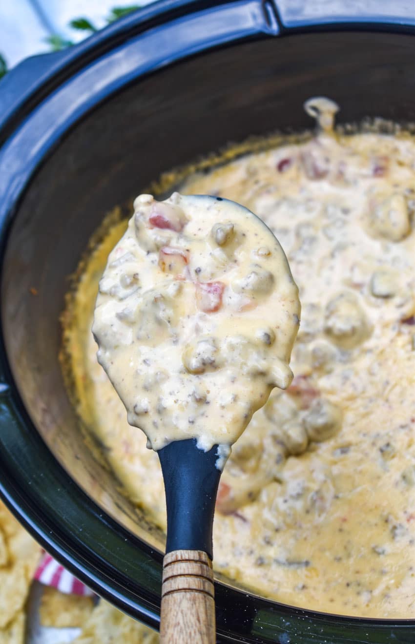 a black spoon holding up a scoop of extra creamy slow cooker queso