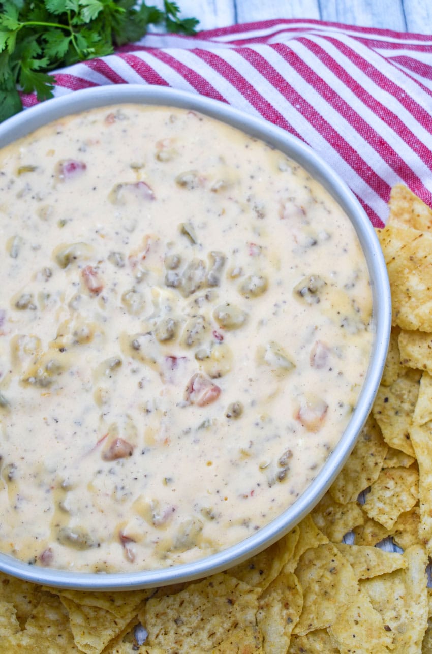 slow cooker queso dip in a white serving bowl surrounded by tortilla chips