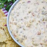 slow cooker queso dip in a white serving bowl surrounded by tortilla chips