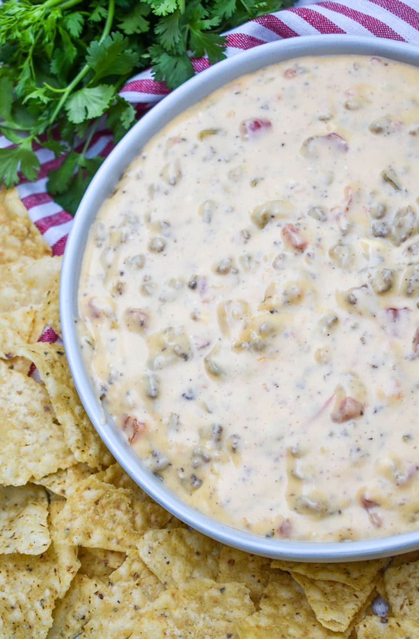 slow cooker queso dip in a white serving bowl surrounded by tortilla chips