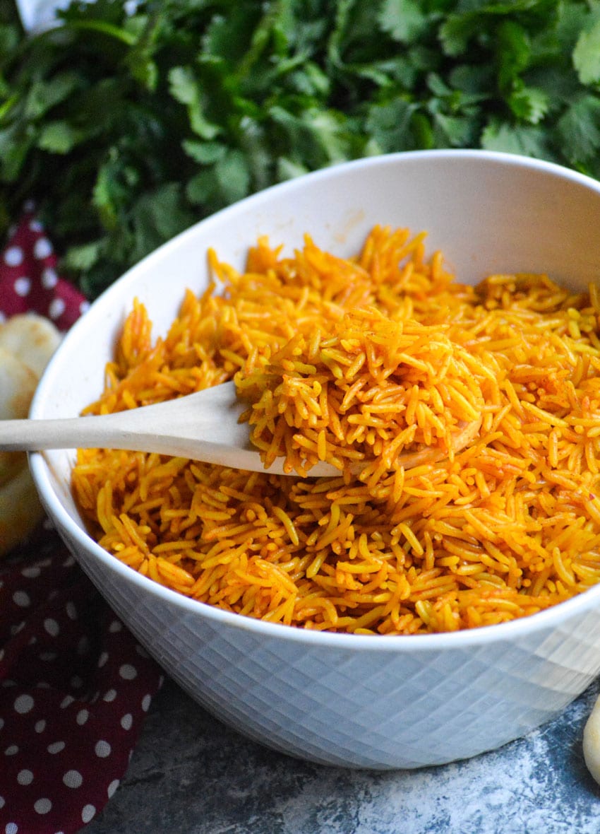 a white spoon lifting tikka masala rice out of a white serving bowl