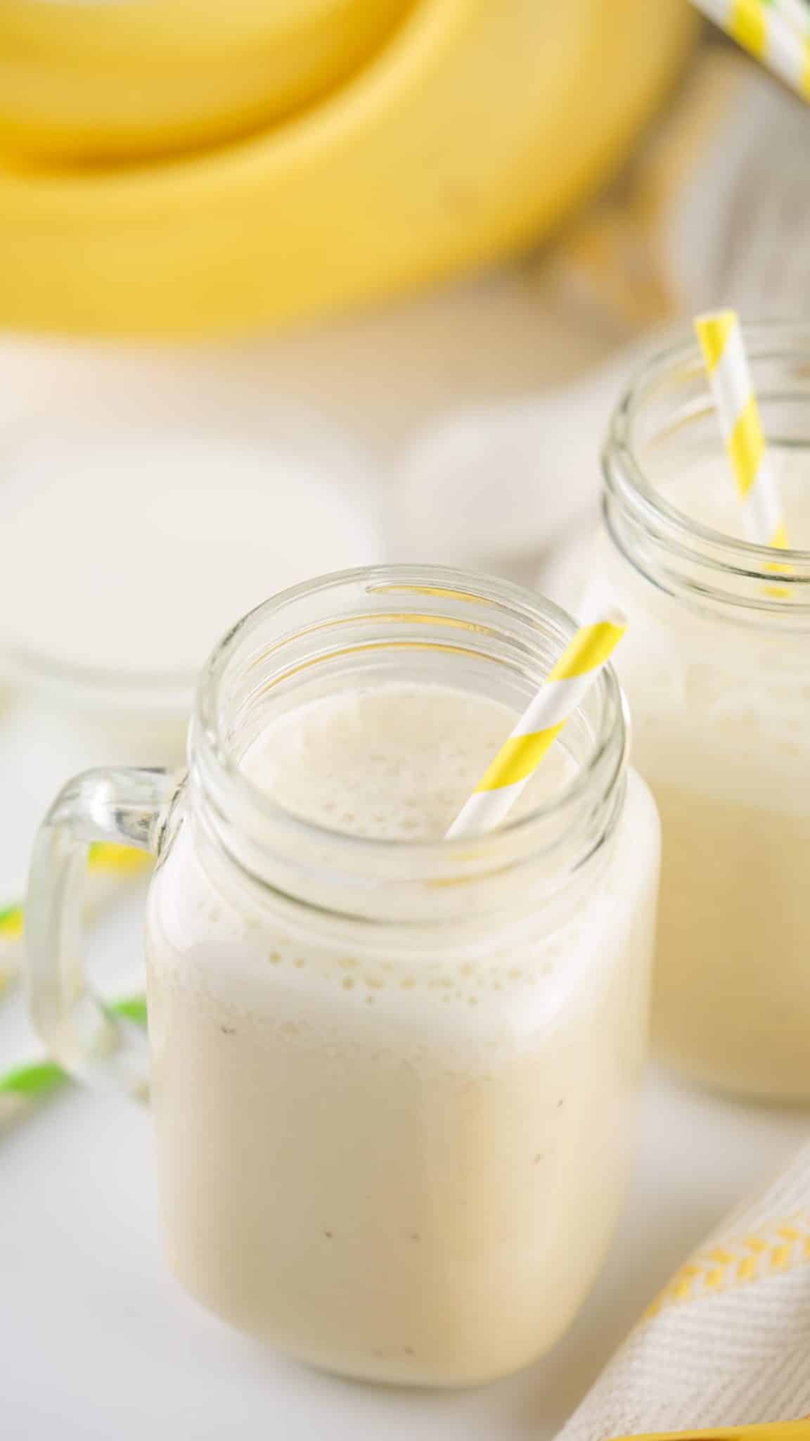 a close up of banana milk in two glass jars with paper straws in them
