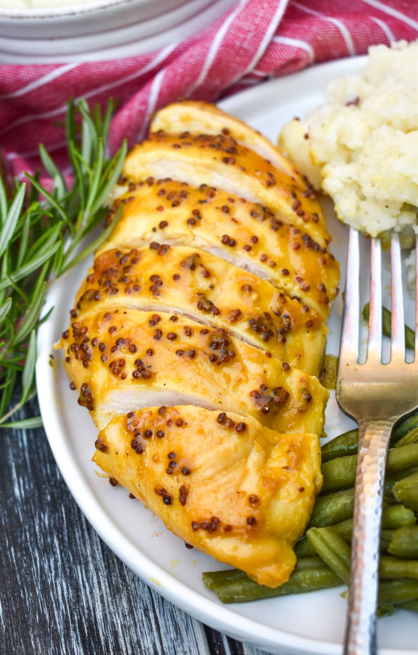 a sliced honey mustard chicken breast on a white plate with mashed potatoes and green beans on the side