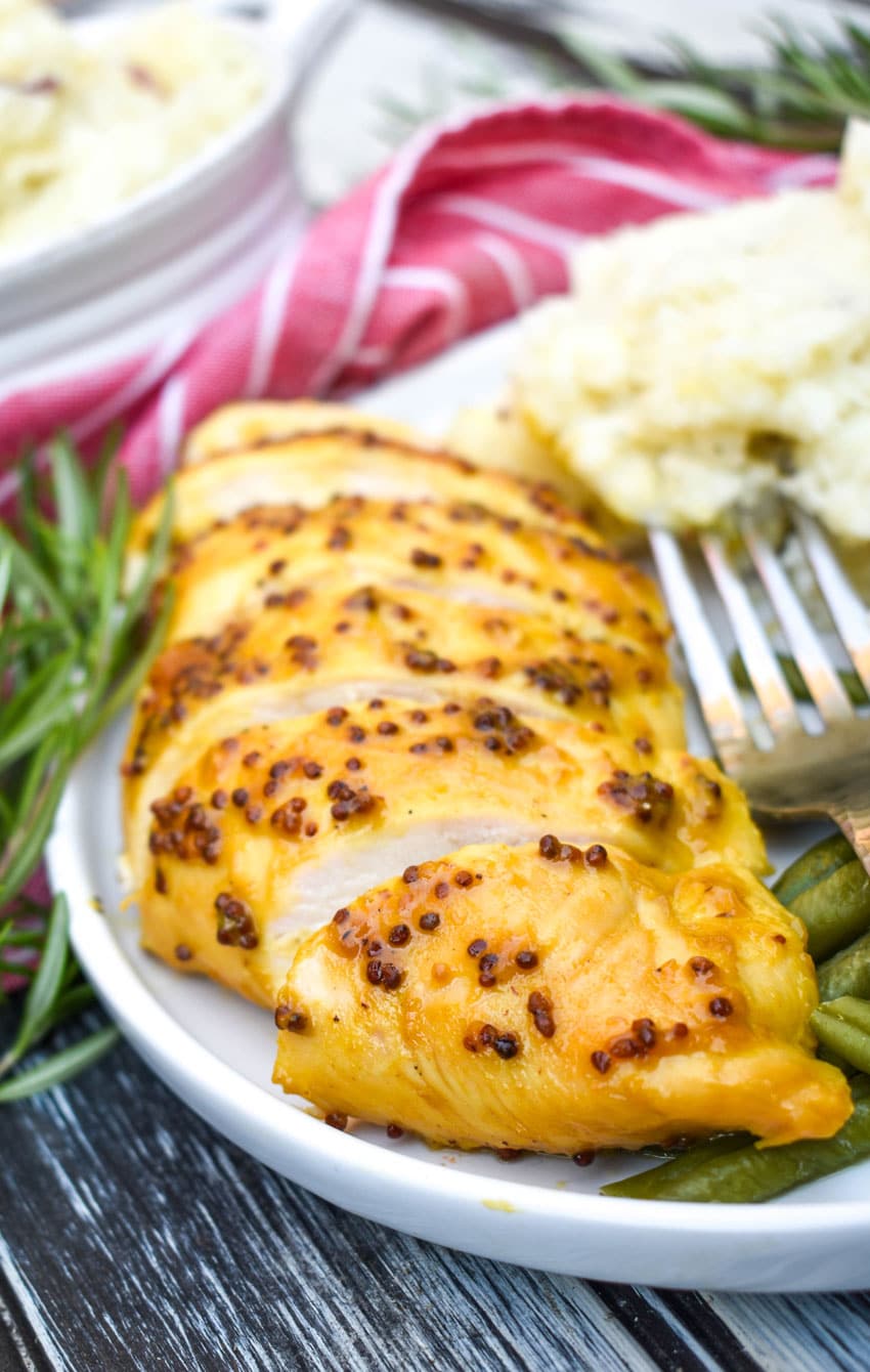 a sliced honey mustard chicken breast on a white plate with mashed potatoes and green beans on the side