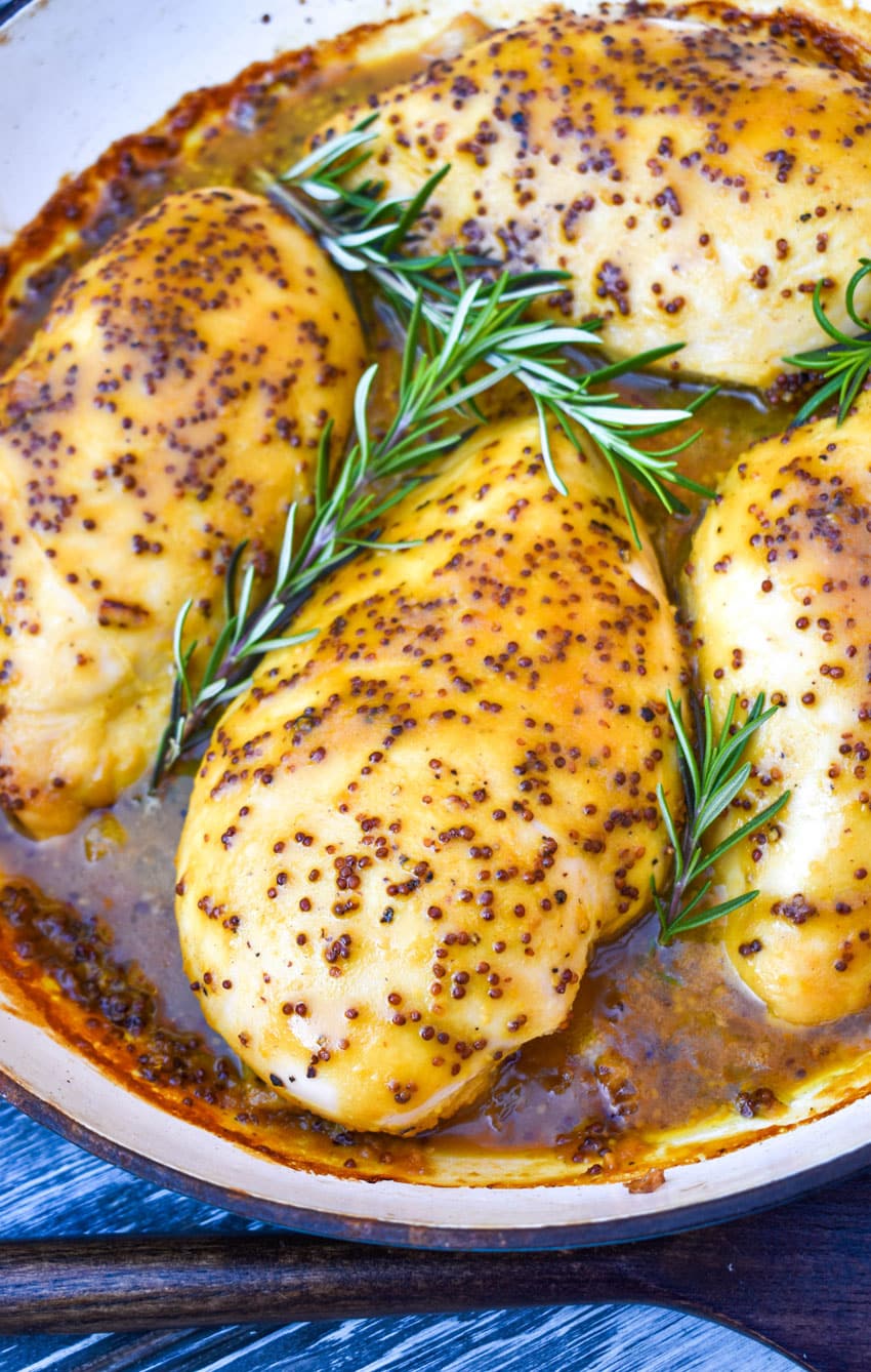 baked honey mustard chicken topped with fresh sprigs of rosemary in a cast iron skillet
