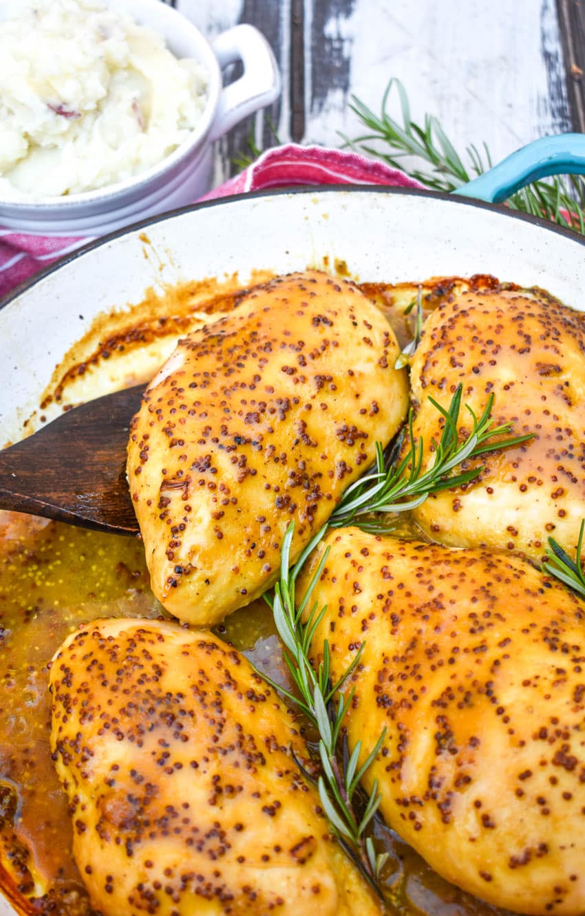 a wooden spatula lifting a piece of baked honey mustard chicken out of a cast iron skillet