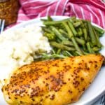 A PIECE OF BAKED HONEY MUSTARD CHICKEN ON A WHITE PLATE WITH MASHED POTATOES AND GREEN BEANS