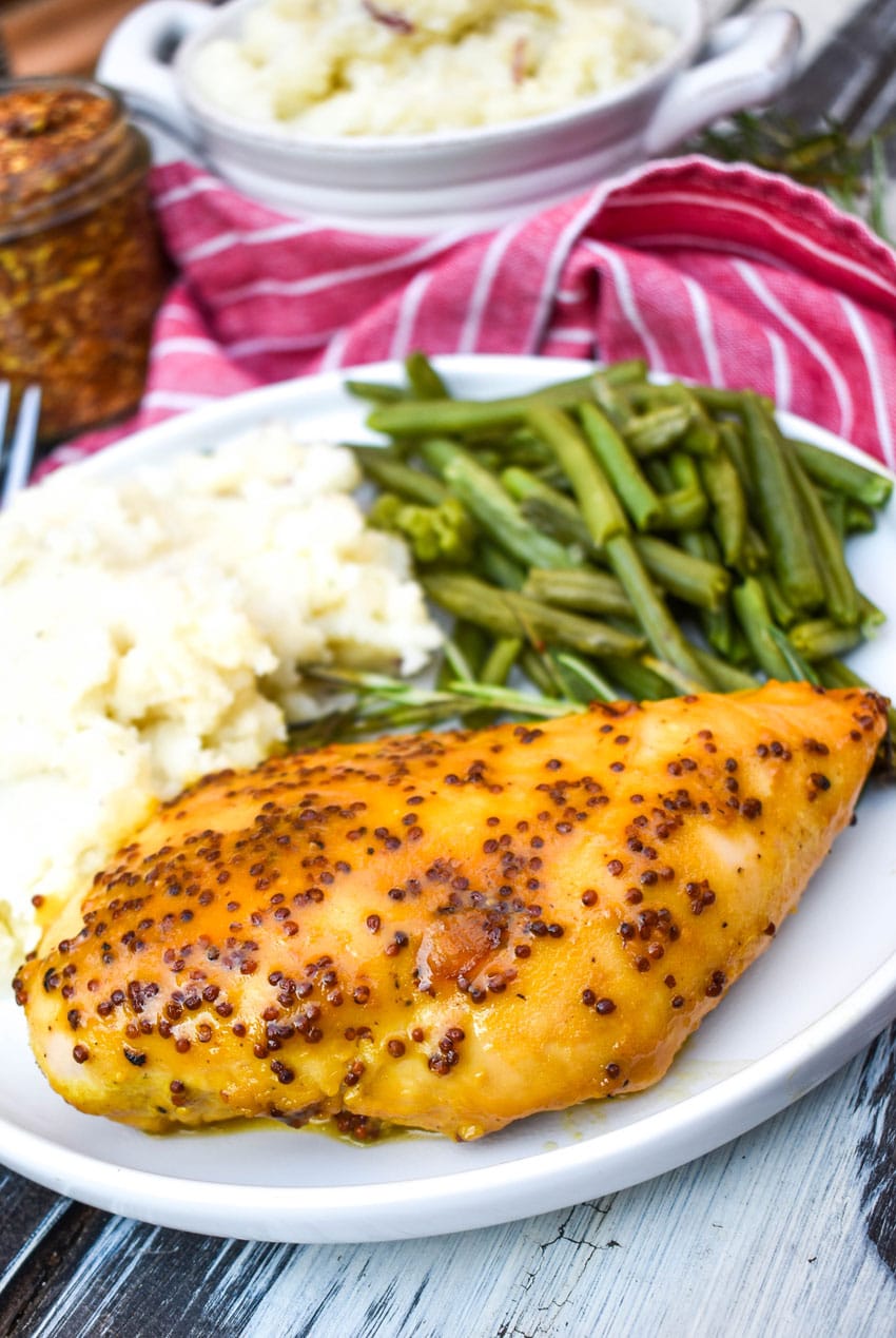 A PIECE OF BAKED HONEY MUSTARD CHICKEN ON A WHITE PLATE WITH MASHED POTATOES AND GREEN BEANS