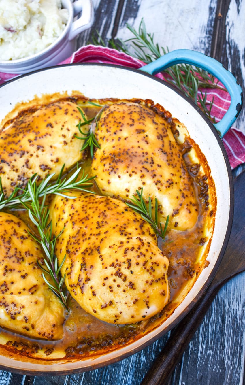 baked honey mustard chicken topped with fresh sprigs of rosemary in a cast iron skillet