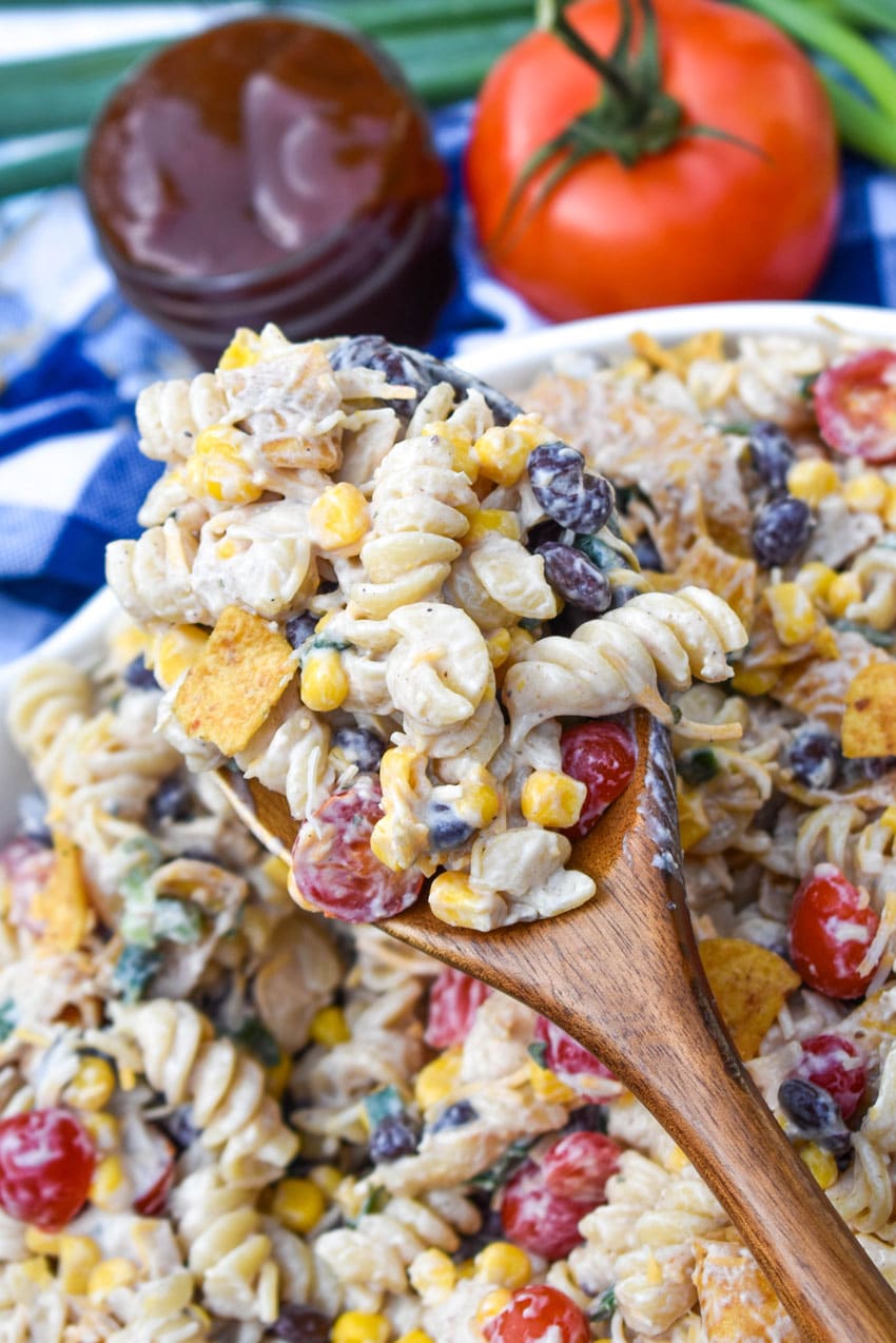 a wooden spoon holding up a scoop of barbecue chicken pasta salad