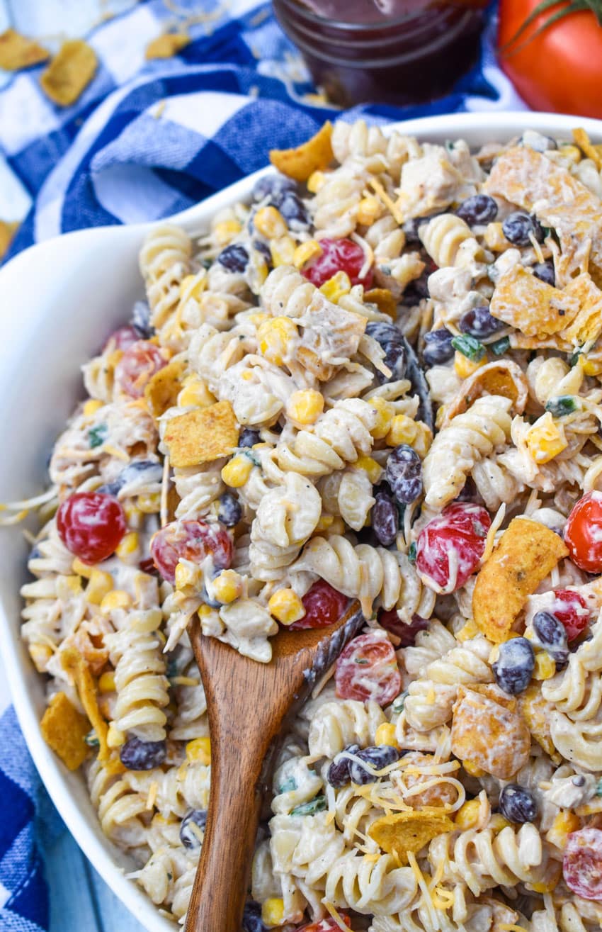 a wooden spoon scooping barbecue chicken pasta salad out of a white serving bowl