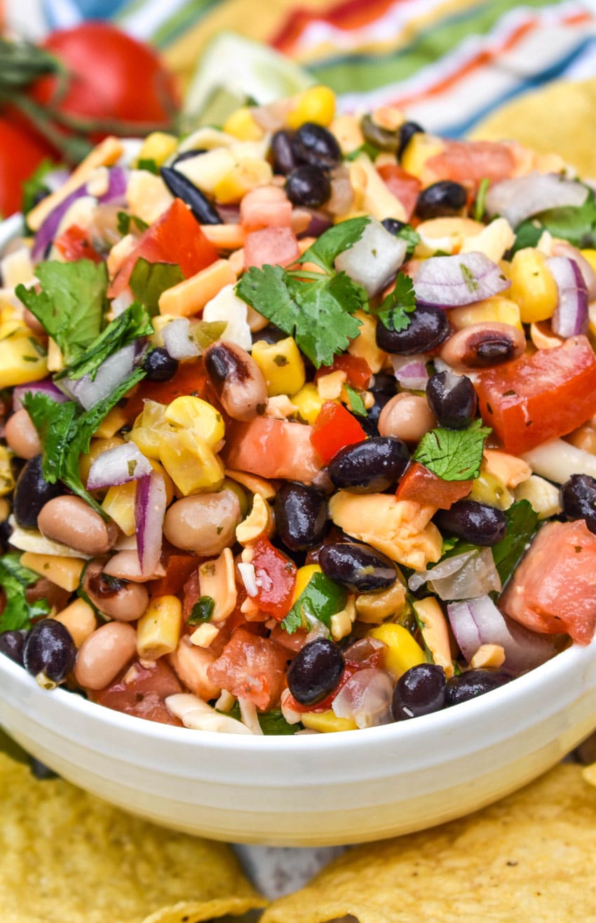 a close up of cowboy caviar dip in a white bowl surrounded by tortilla chips