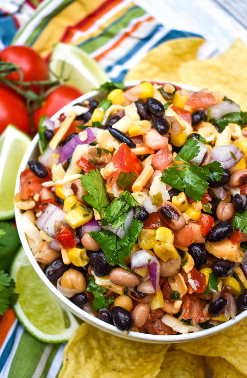 a close up of cowboy caviar dip in a white bowl surrounded by tortilla chips