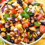 a close up of cowboy caviar dip in a white bowl surrounded by tortilla chips