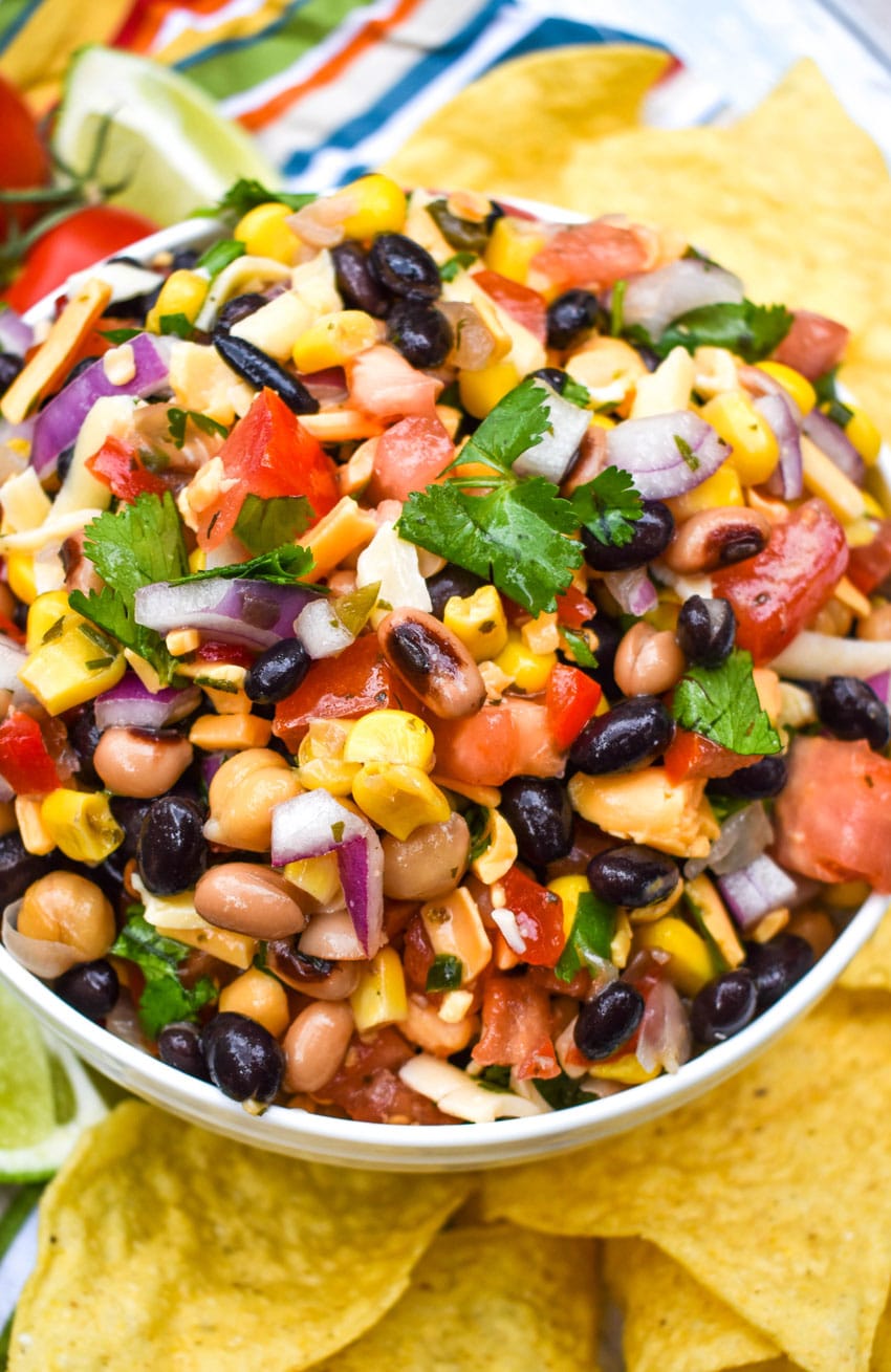 a close up of cowboy caviar dip in a white bowl surrounded by tortilla chips