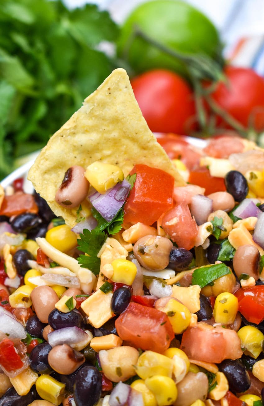 a tortilla chip scooping cowboy caviar out of a white bowl