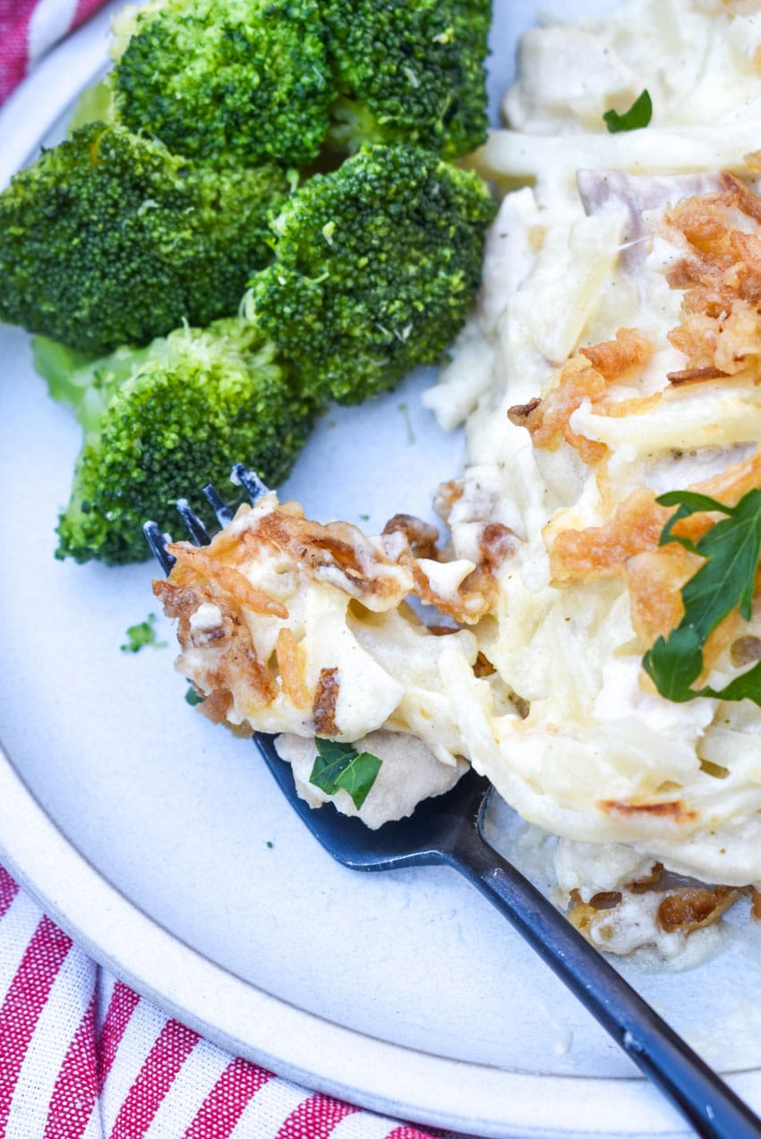 a black fork scooping french onion chicken casserole off a small white dinner plate