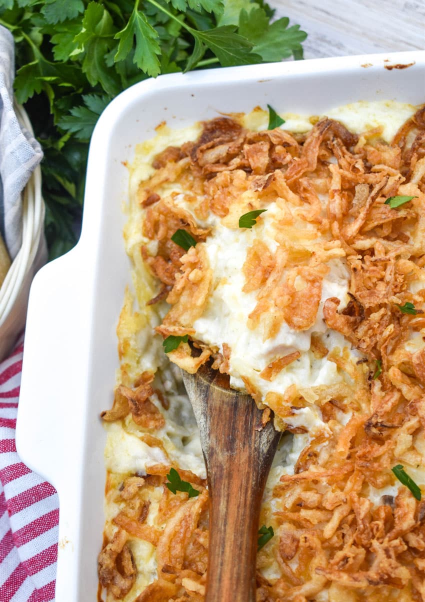 a wooden spoon scooping french onion chicken casserole out of a white baking dish