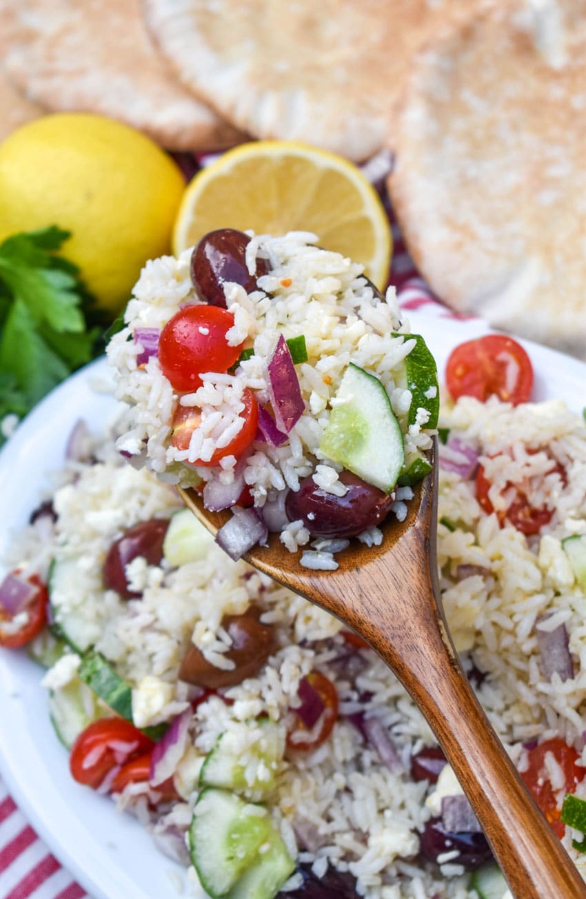 a wooden spoon holding up a scoop of greek rice salad