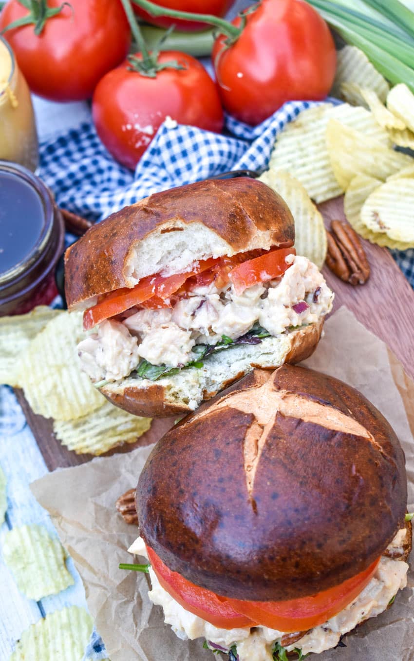 honey mustard chicken salad sandwich on pretzel buns on a wooden cutting board