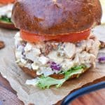 honey mustard chicken salad sandwich on pretzel buns on a wooden cutting board
