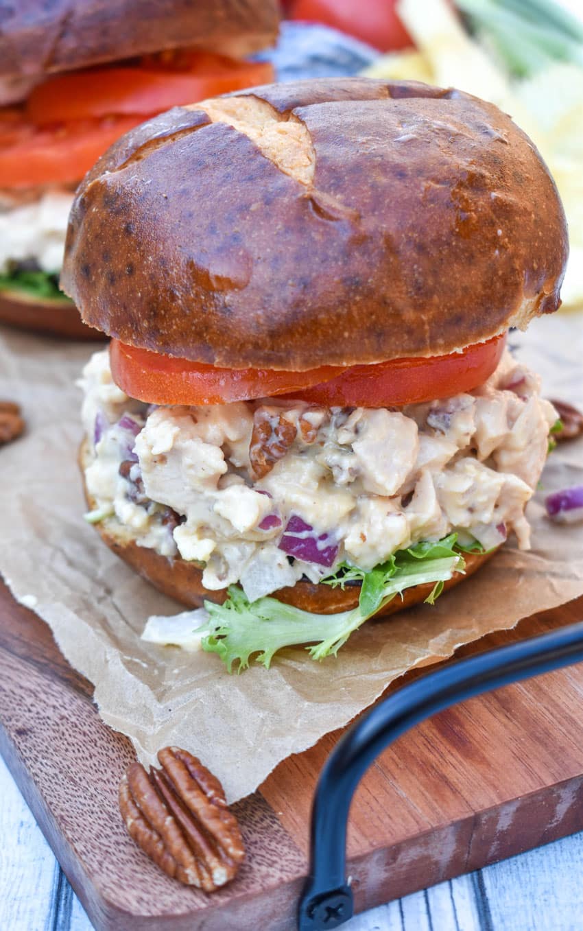honey mustard chicken salad sandwich on pretzel buns on a wooden cutting board