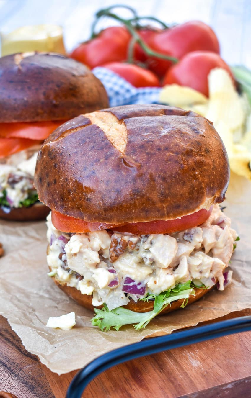 honey mustard chicken salad sandwich on pretzel buns on a wooden cutting board