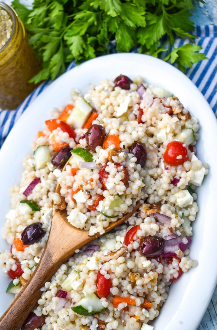 a wooden spoon scooping Mediterranean couscous salad out of a white serving bowl