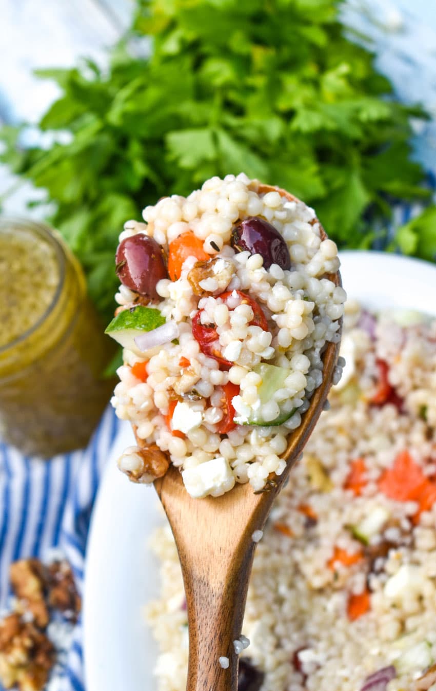 a wooden spoon holding up a scoop of Mediterranean couscous salad