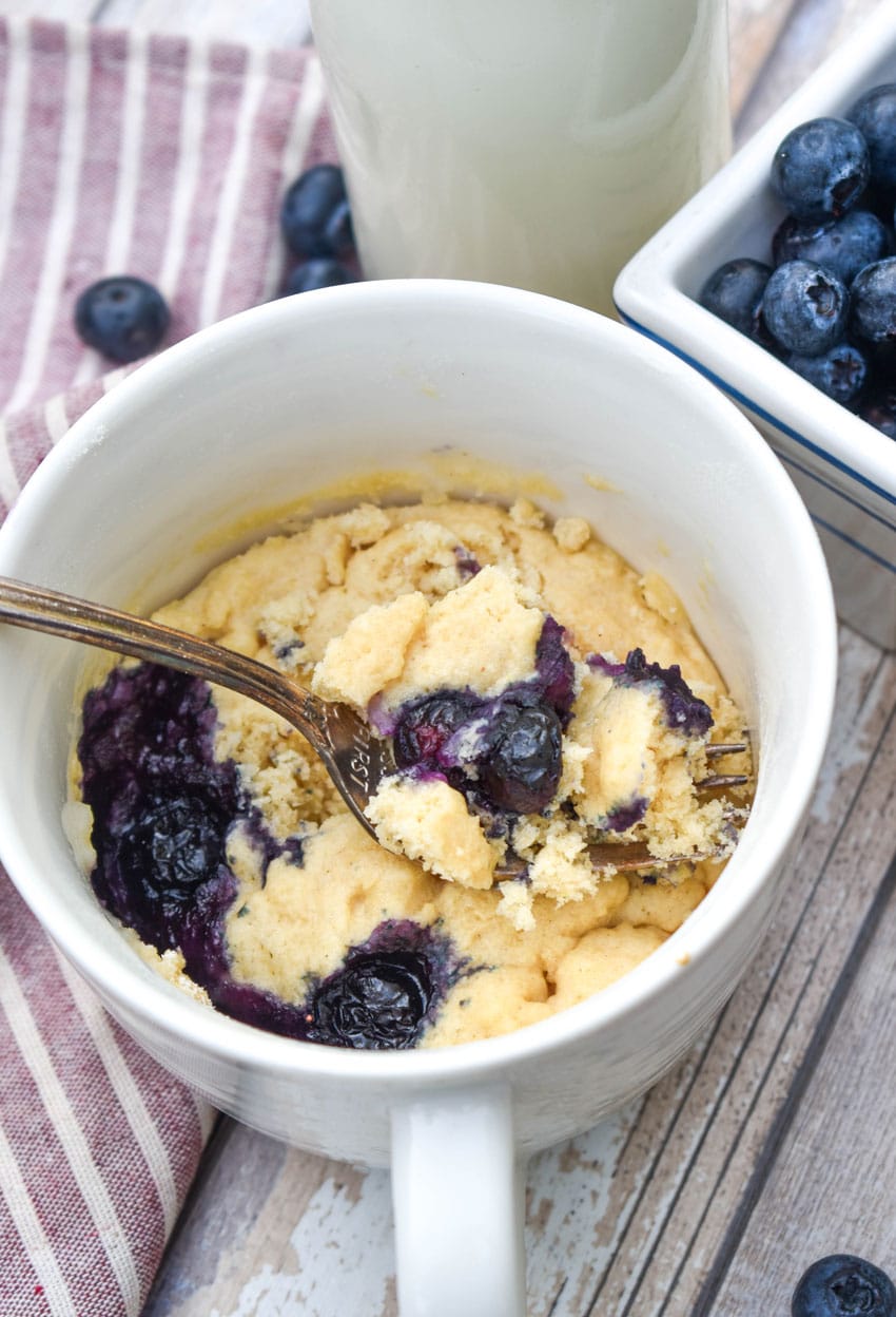 a silver fork scooping microwave blueberry muffin mug cake out of a white mug