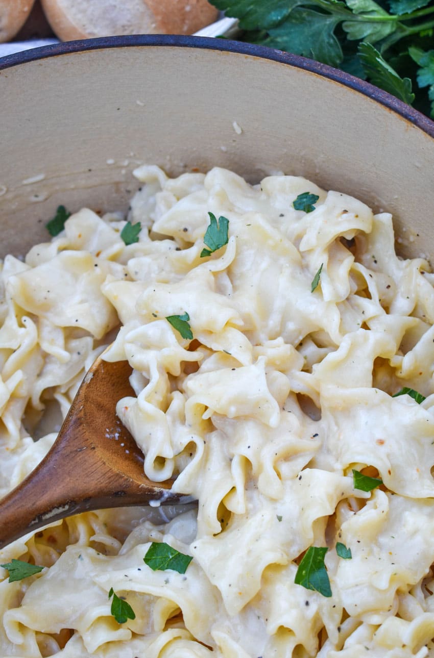 a wooden spoon scooping creamy italian noodles out of a large pot