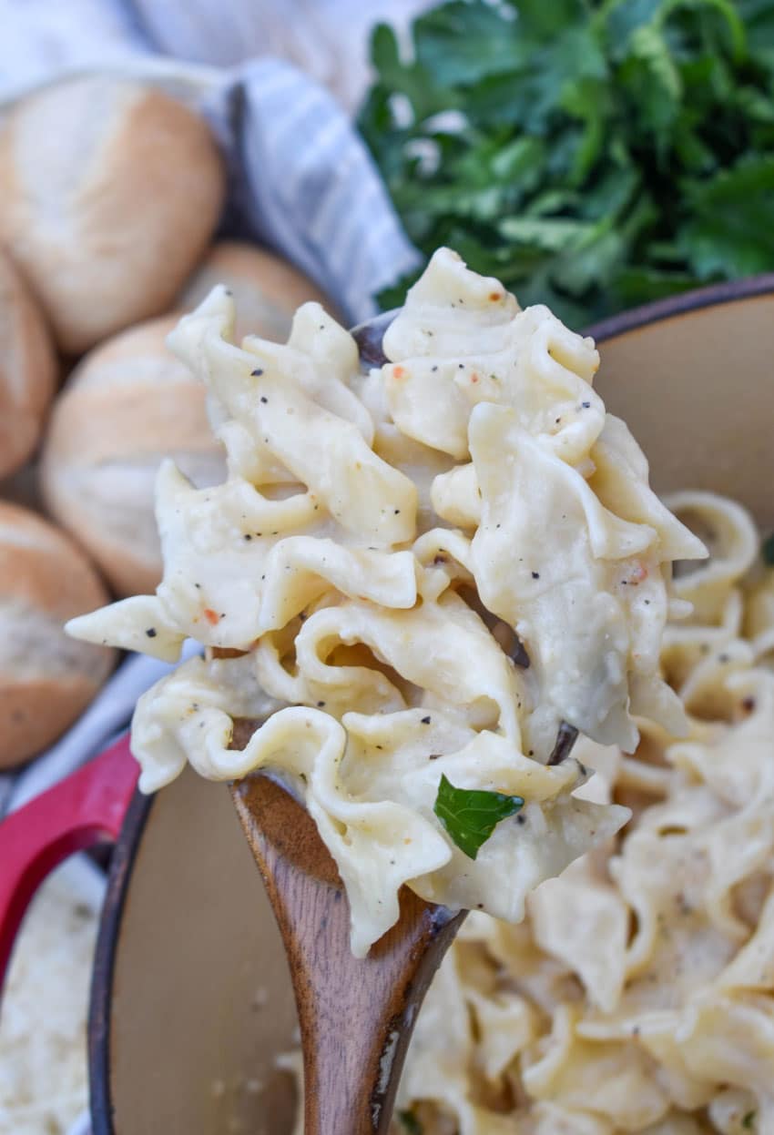 a wooden spoon holding up a scoop of creamy italian noodle pasta