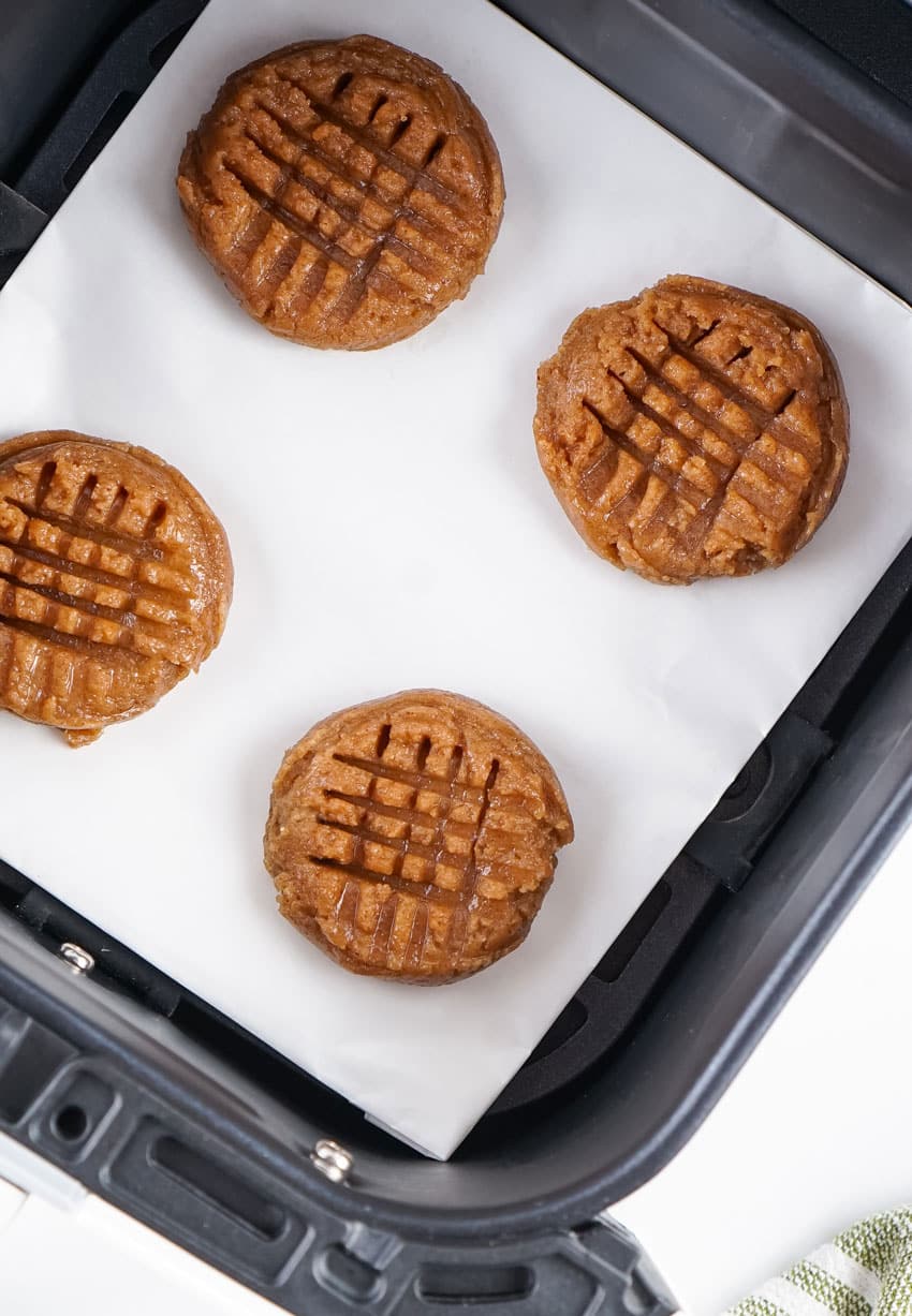 four unbaked almond butter cookies on parchment paper in the basket of an air fryer