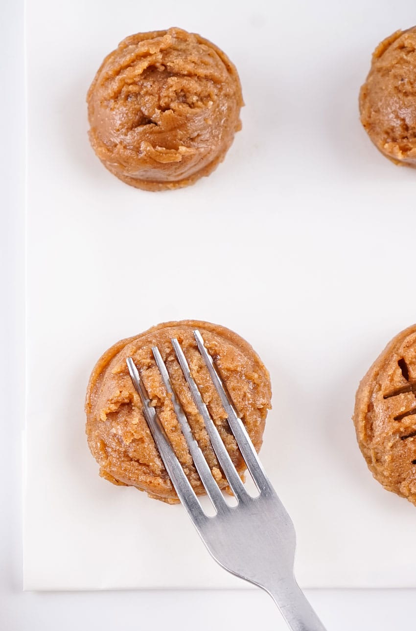 a silver fork pressing lines into almon butter cookie dough balls