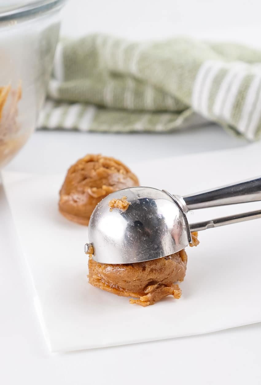 a small cookie scoop scooping almond butter cookie dough onto a white piece of parchment paper