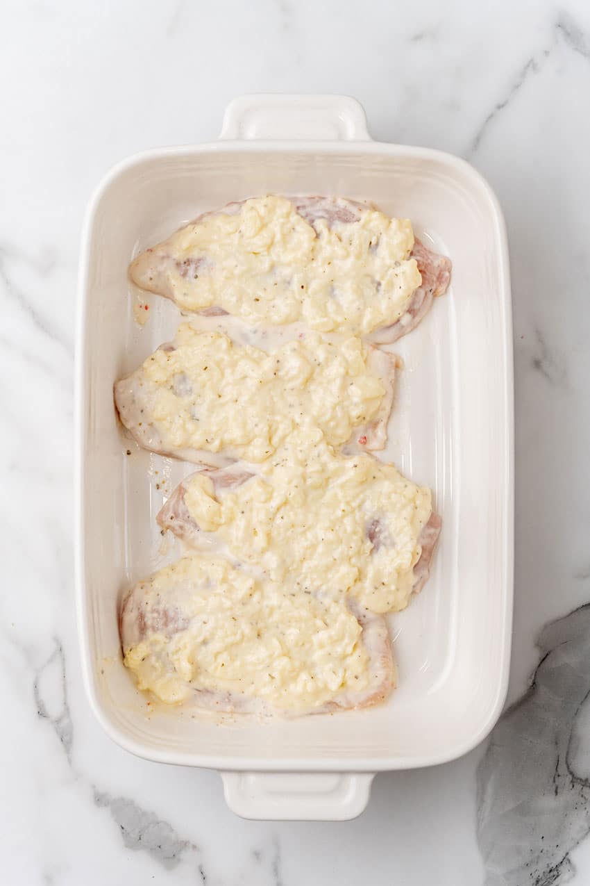 ranch dressing spread over chicken breasts in a white baking dish