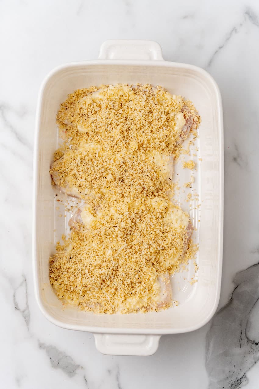 parmesan crusted chicken arranged in a row in a white baking dish