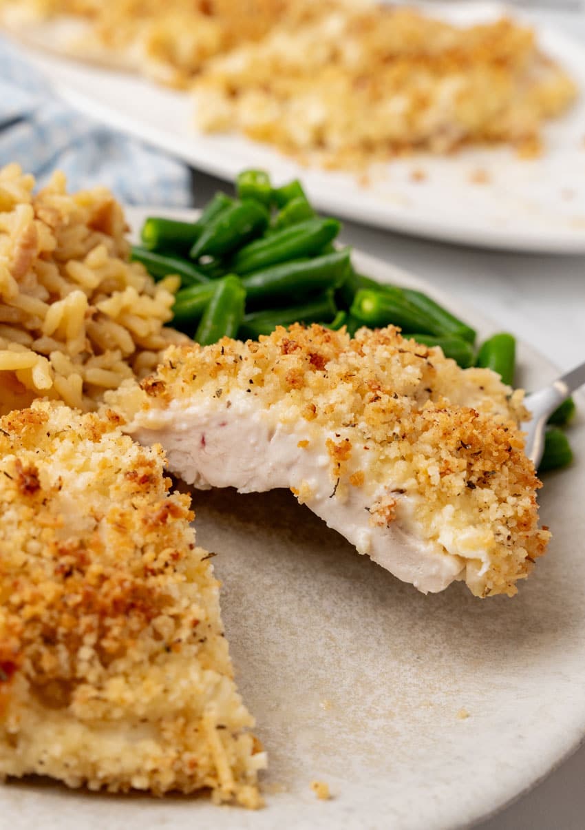a cut piece of parmesan crusted chicken being lifting off a white plate by a fork