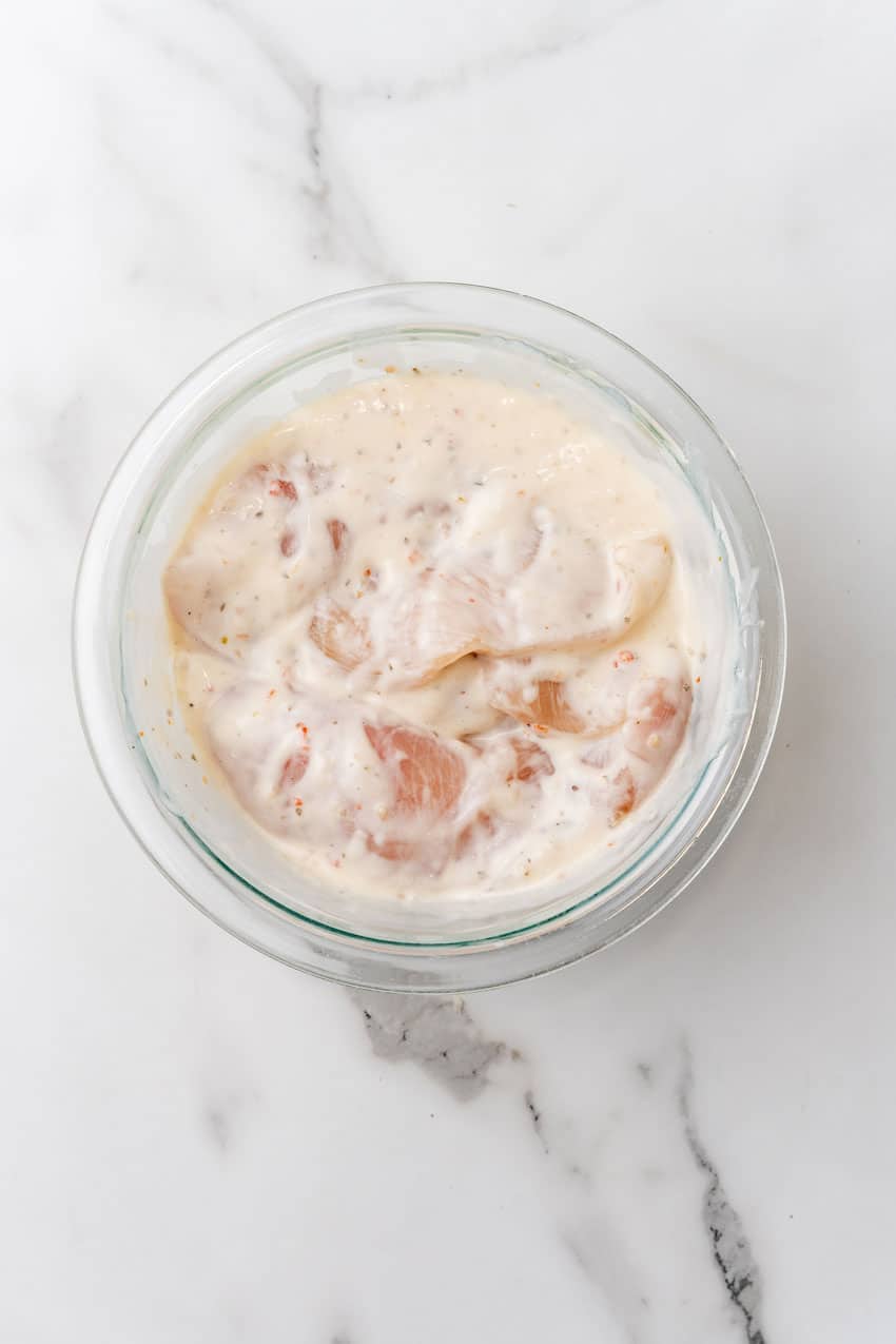 chicken breasts marinading in a creamy sauce in a glass mixing bowl