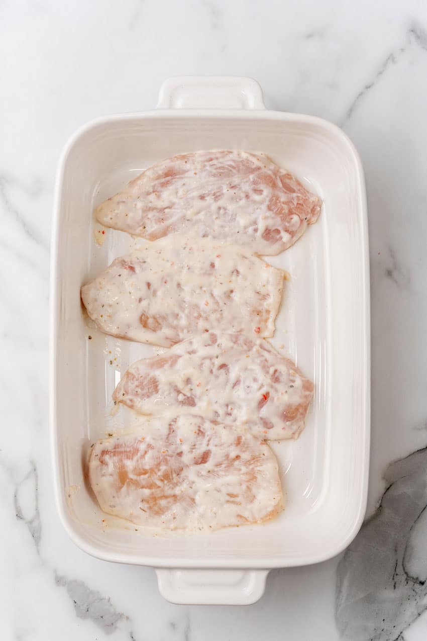 marinaded chicken breasts arranged in a row in a white baking dish