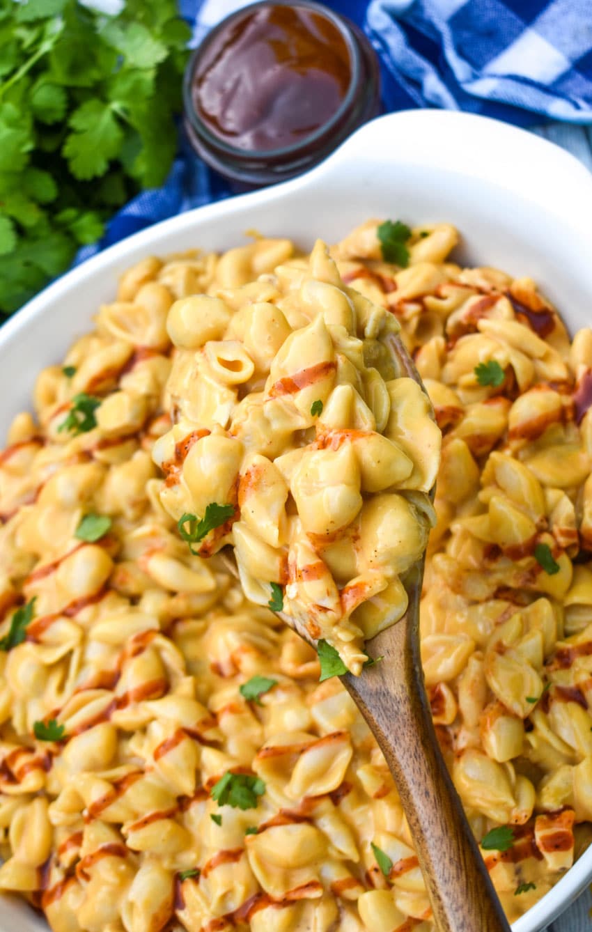 a wooden spoon scooping barbecue chicken mac and cheese out of a white serving bowl