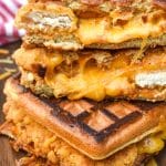 chicken and waffle grilled cheese sandwiches stacked on a wooden cutting board