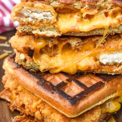 chicken and waffle grilled cheese sandwiches stacked on a wooden cutting board