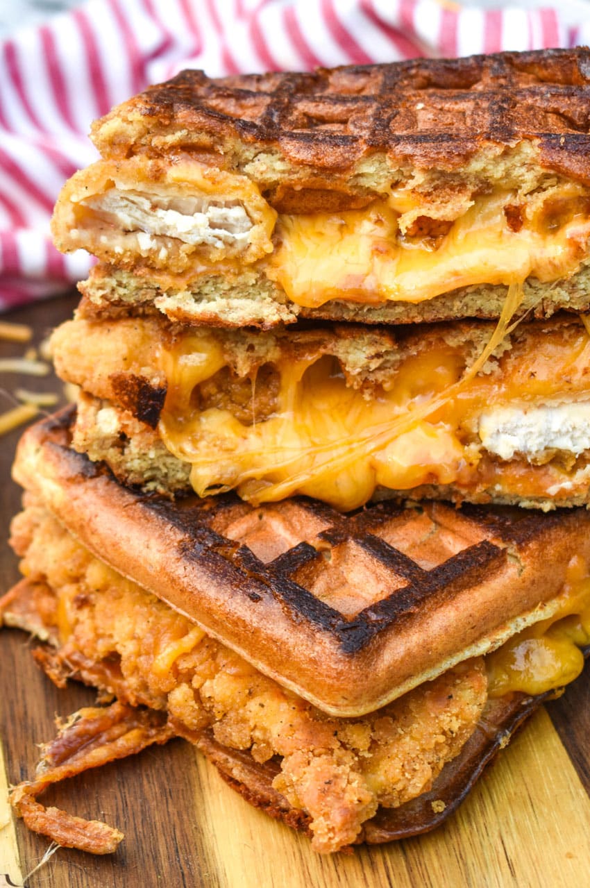 chicken and waffle grilled cheese sandwiches stacked on a wooden cutting board