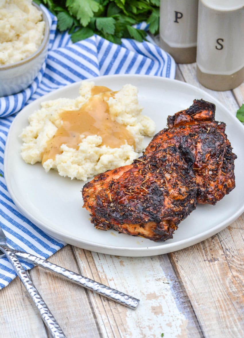air fried crispy chicken thighs on a white plate with mashed potatoes and gravy on the side