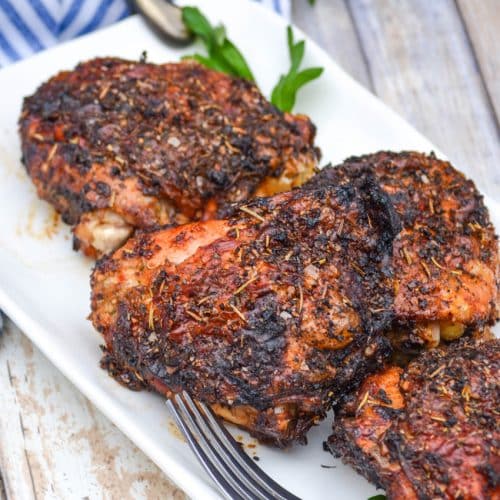 air fried crispy chicken thighs on a white serving platter with fresh herbs in the background