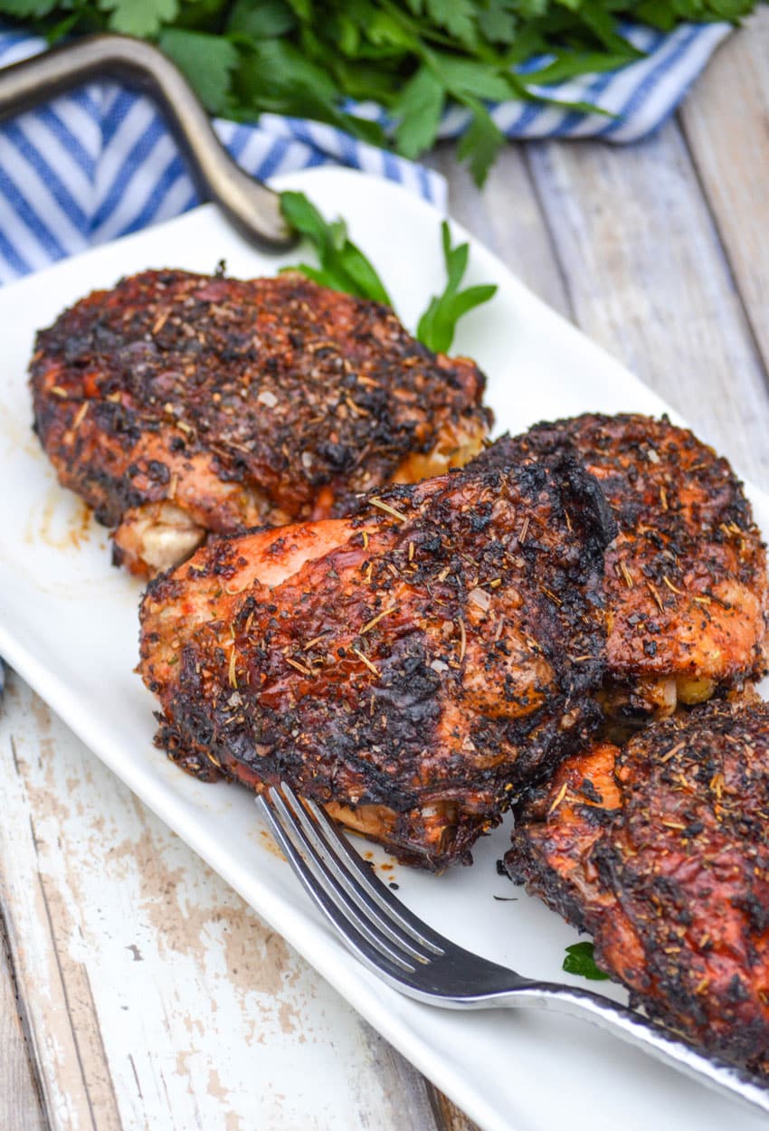 Crispy Chicken Thighs (Air Fryer Recipe) air fried crispy chicken thighs on a white serving platter with fresh herbs in the background