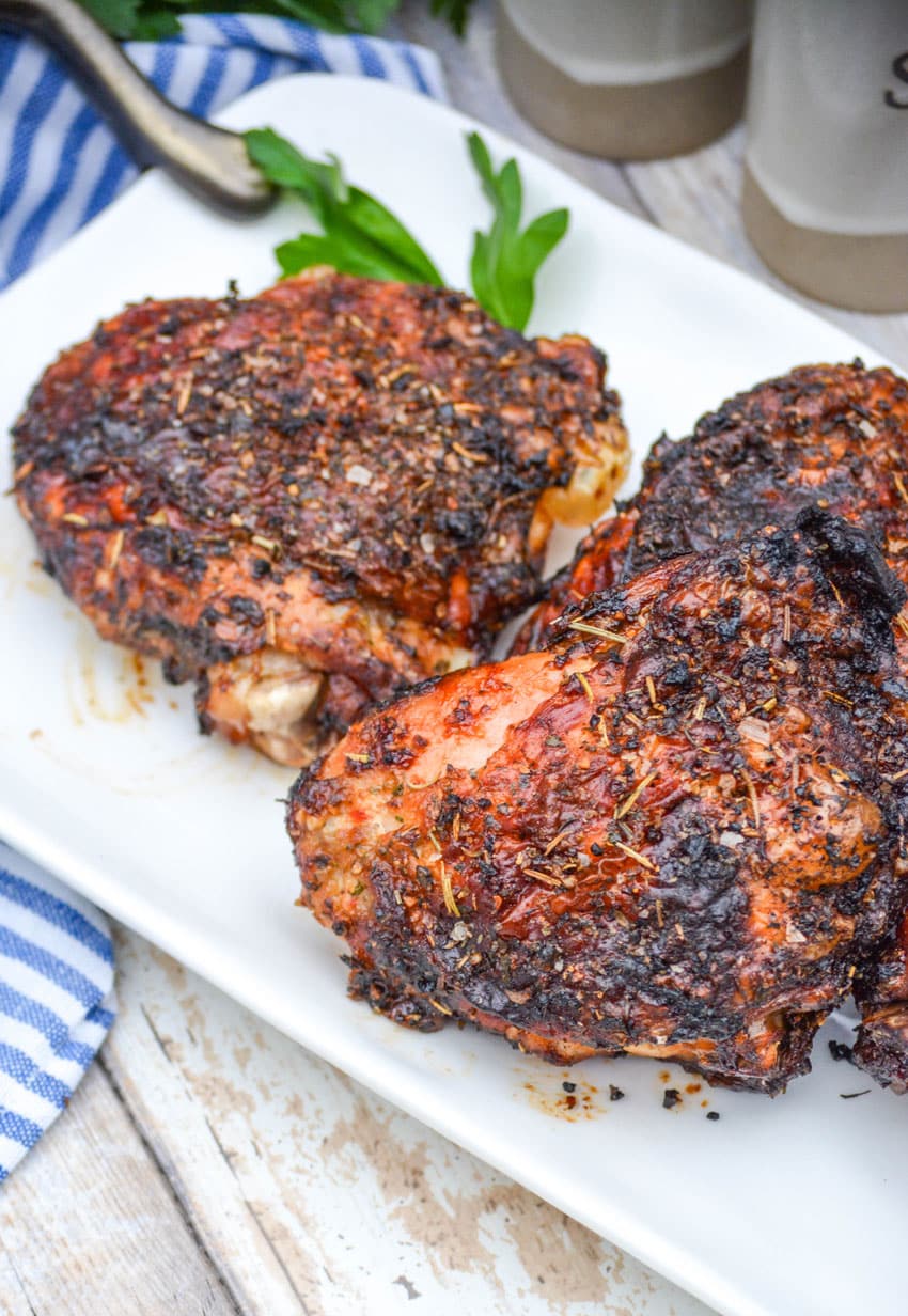 air fried crispy chicken thighs on a white serving platter with fresh herbs in the background
