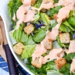 homemade thousand island dressing drizzle over chopped lettuce in a white serving bowl