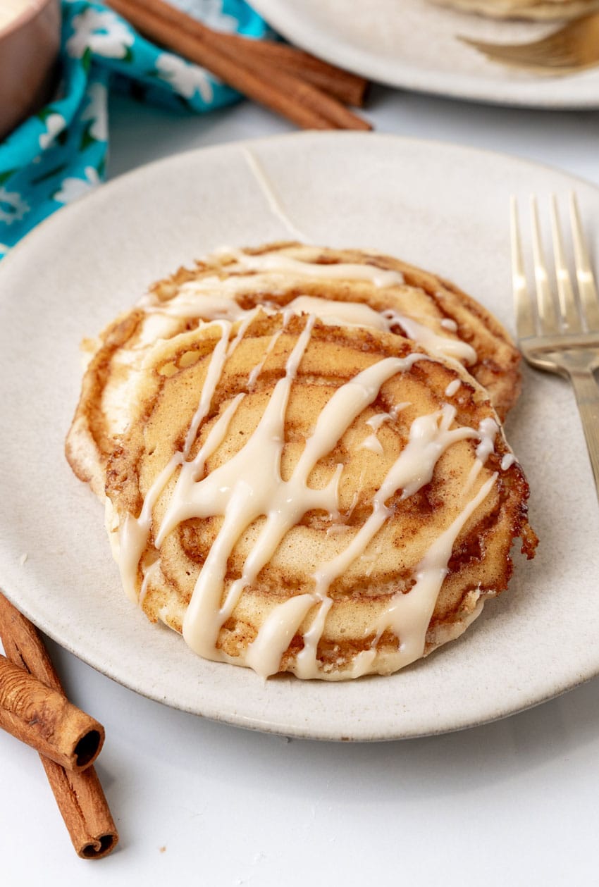 two cinnamon roll pancakes on a white plate with a silver fork resting on the side